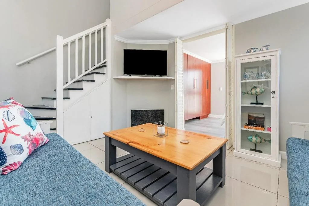 Open-plan lounge with blue sofas, wooden coffee table, and wall-mounted TV