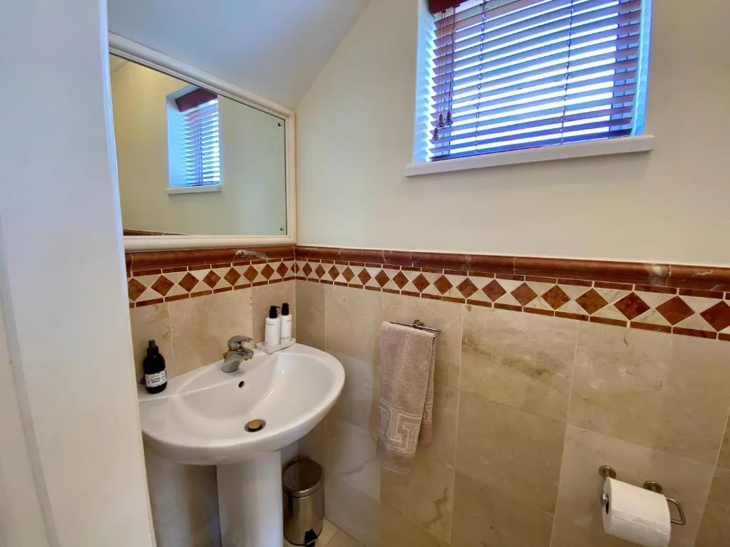 Bathroom with pedestal sink, decorative tile border, and window blinds