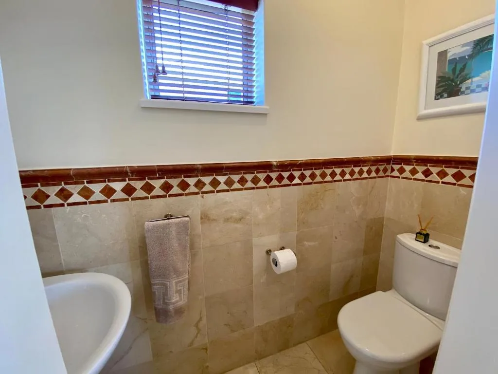 Bathroom with beige tile walls, decorative border trim, toilet and sink