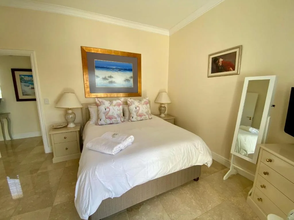 Bright bedroom with queen bed, cream bedding, and framed coastal artwork