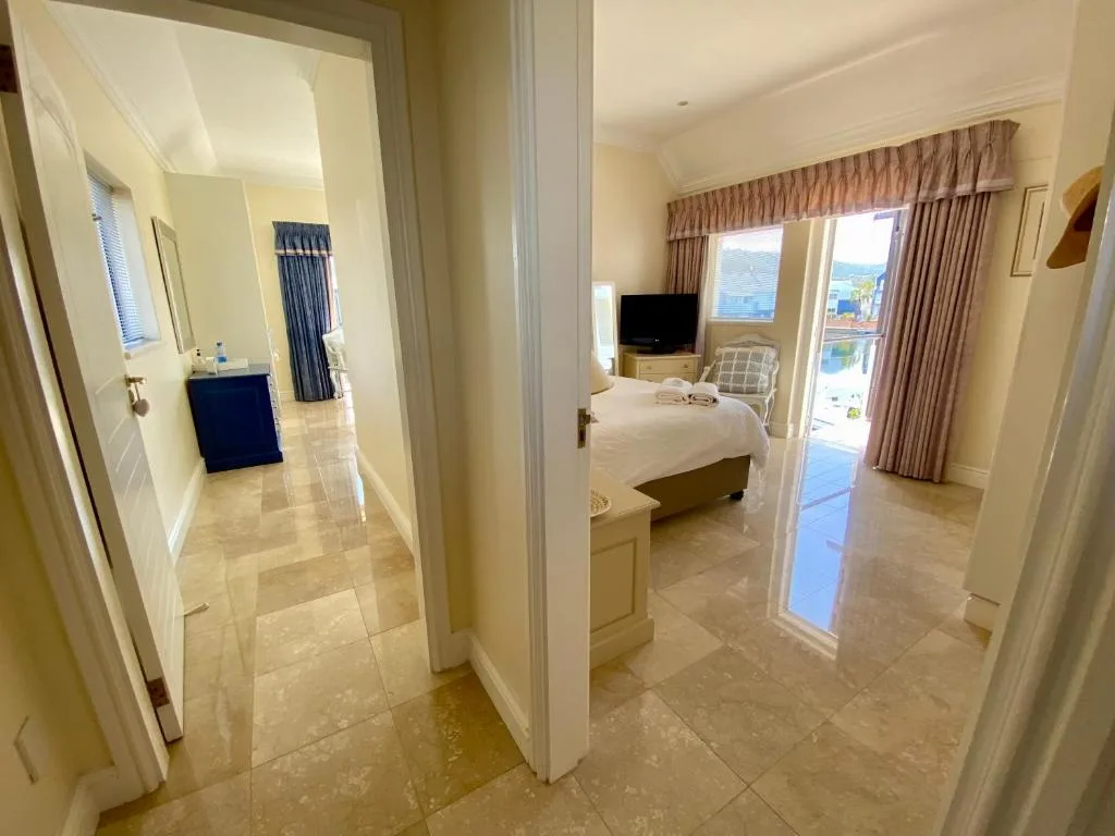 Master bedroom with en-suite bathroom, bed, TV, and lagoon views through patio doors