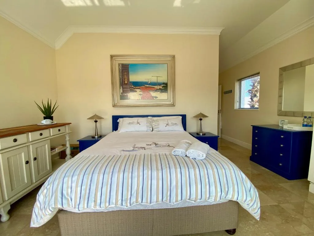 Spacious bedroom with blue bed frame and striped bedding, coastal artwork overhead