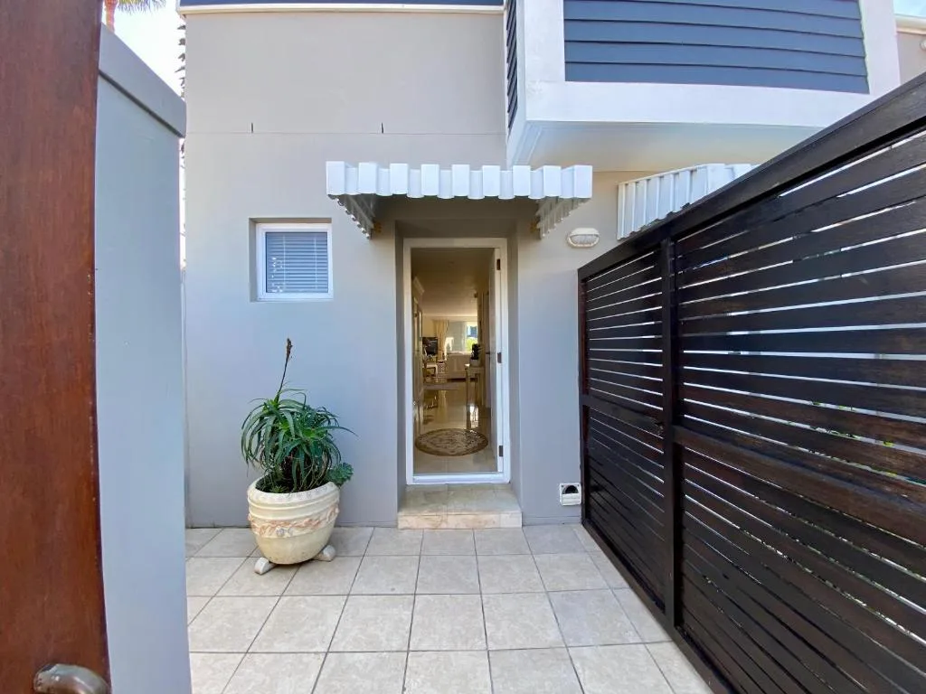 Modern white entrance with dark gate, potted plant, and tiled courtyard