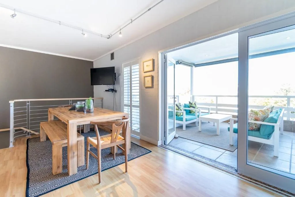 Modern dining area with wooden table, chairs, and open deck access