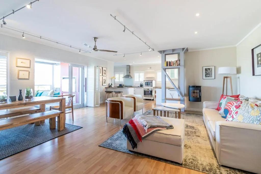 Bright open-plan lounge with cream sofas, wooden dining table, and kitchen visible beyond