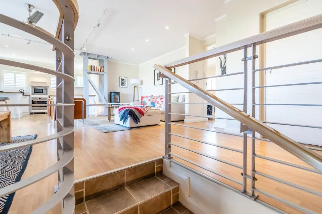 Modern open-plan lounge with sofa, wooden flooring, and metal staircase railing