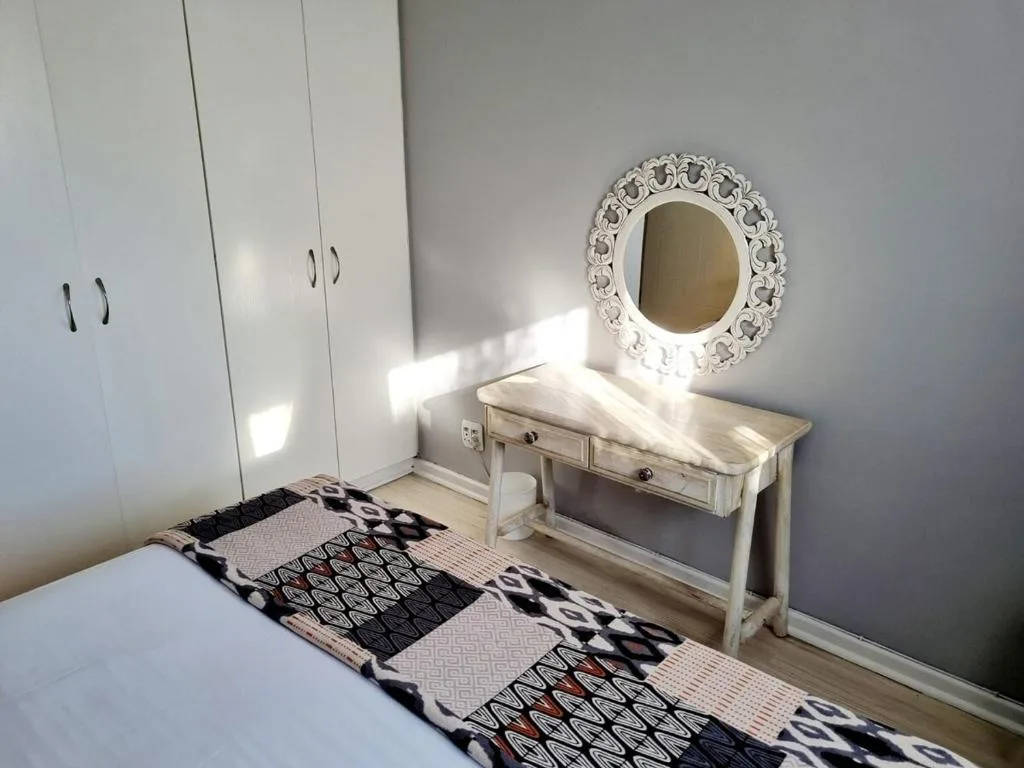 Bright bedroom with bed, white wardrobe, and decorative mirror on wall