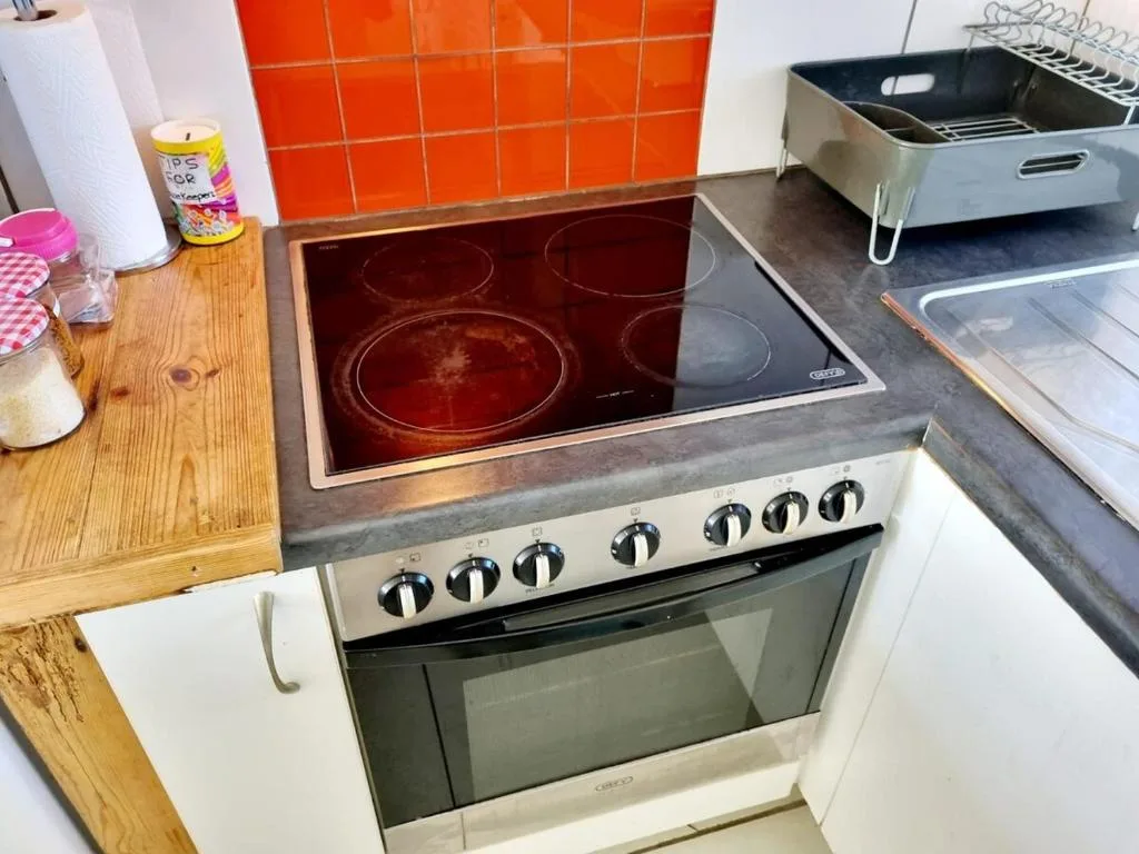 Electric cooktop and oven with red tile backsplash in compact kitchen