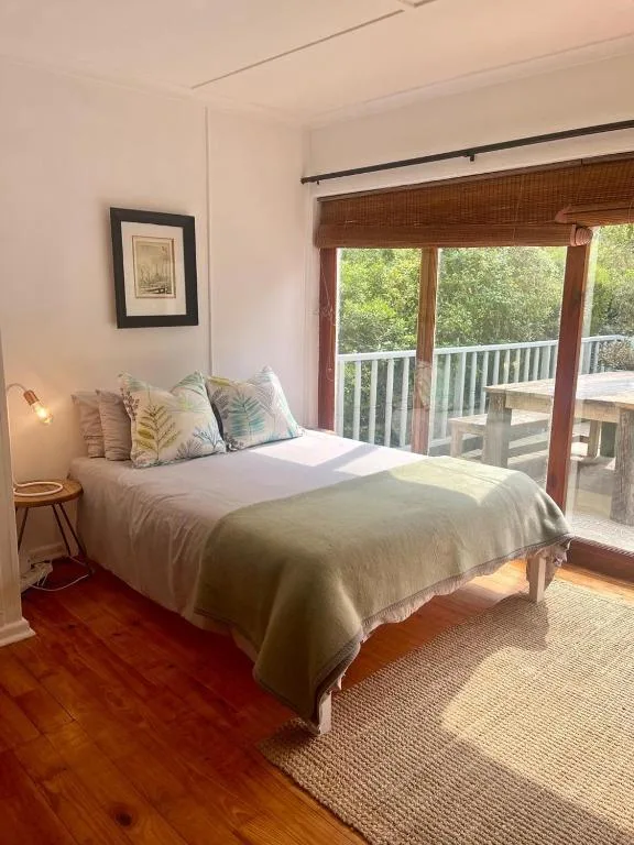 Bright bedroom with made bed, garden-view doors, and wooden flooring
