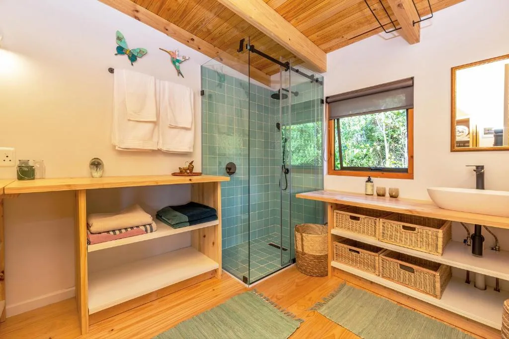 Modern bathroom with green tiled shower, wooden beams, double vanity, and storage baskets