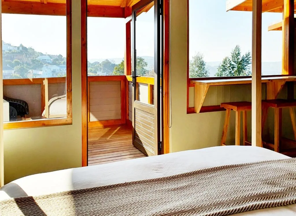 Modern bedroom with bed, wooden deck, and scenic valley views through glass doors