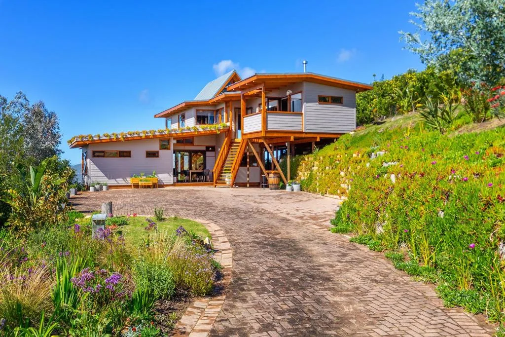 Modern elevated house with wooden trim, brick driveway, and flowering garden landscaping