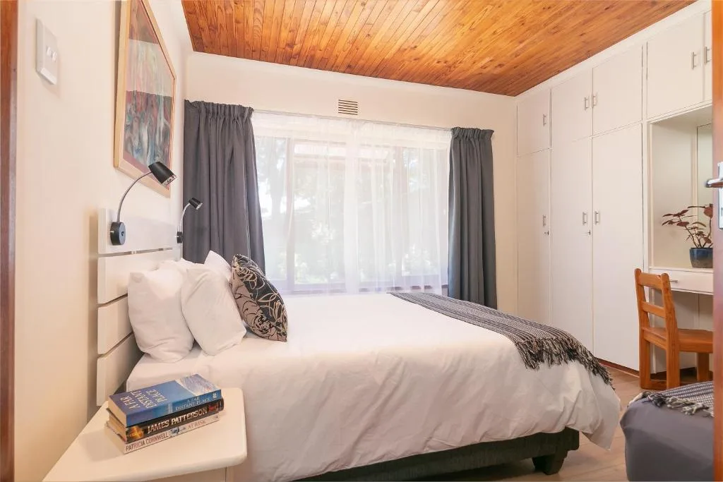 Bright bedroom with white bedding, wooden ceiling, and garden views through curtains