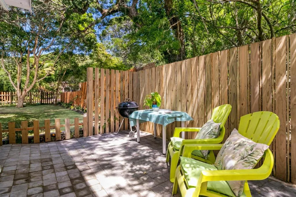 Patio area with green Adirondack chairs, braai grill, and wooden fence
