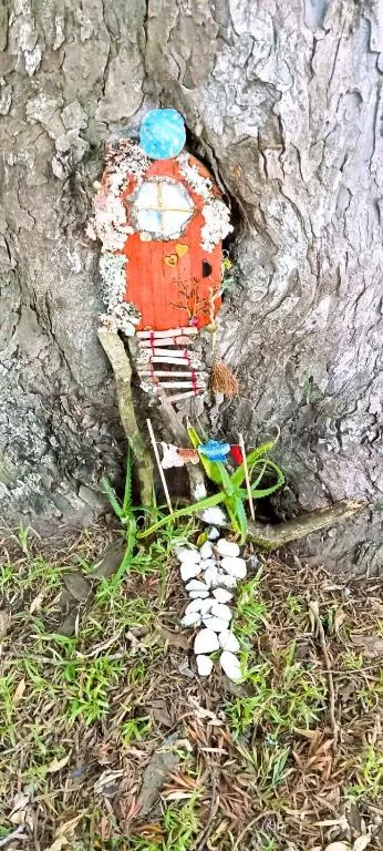 Whimsical painted rock figure on tree bark with colorful decorations