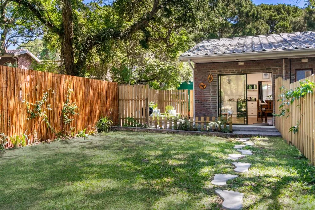 Brick cottage with manicured lawn, wooden fencing, and shaded garden area