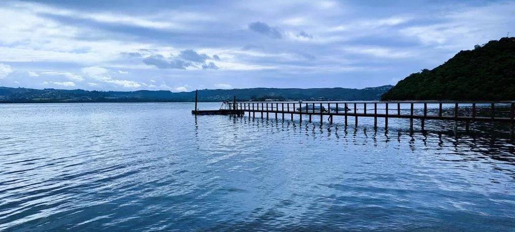 Calm lagoon with wooden jetty and distant forested mountains under blue sky