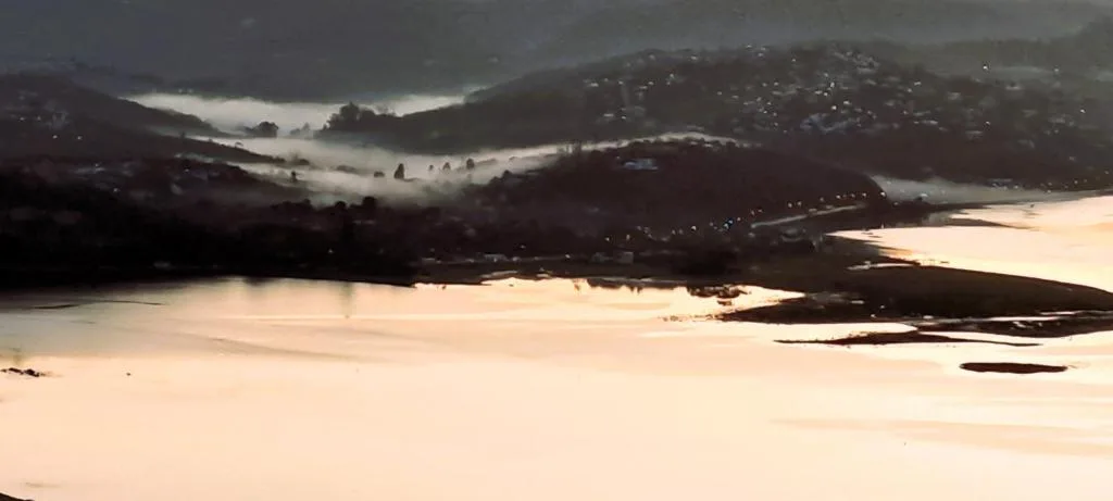 Expansive lagoon and mountain landscape at sunrise with misty peaks