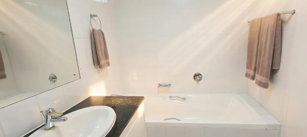 Modern bathroom with white basin, mirror, bathtub and soft towels