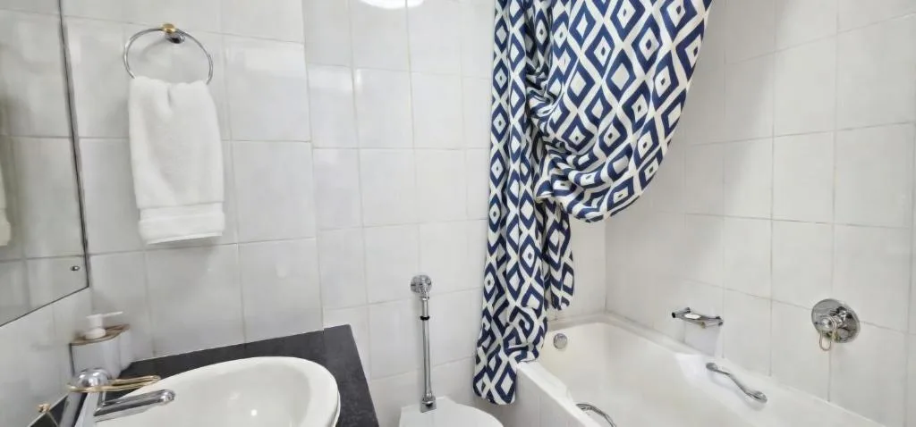 Clean white bathroom with round sink, bathtub, and geometric patterned towel