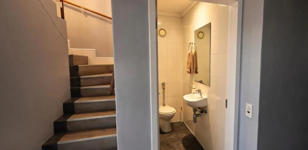Compact bathroom with toilet, sink, mirror, and tiled walls