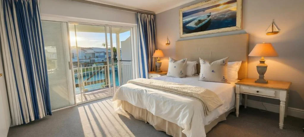 Bright bedroom with double bed, ocean view through glass doors, warm lighting