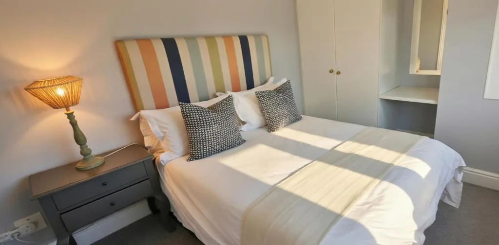 Bright bedroom with colorful striped headboard and white bedding, bedside lamp