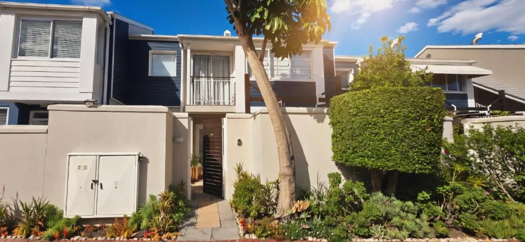 Modern townhouse facade with palm tree, manicured hedges, and entrance pathway