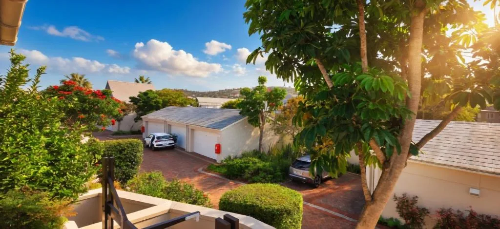 Modern white house with driveway, parked cars, and lush garden landscaping