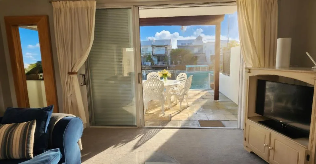 Bright lounge with blue armchair, TV, and pool view through sliding doors