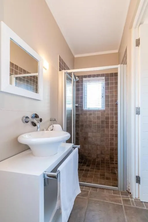 Modern bathroom with round white sink, mirror, and enclosed shower with brown tile