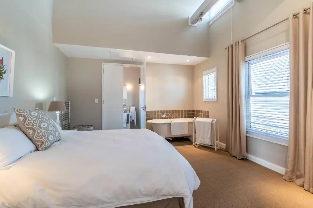 Spacious bedroom with queen bed, ensuite bathroom visible, bright windows