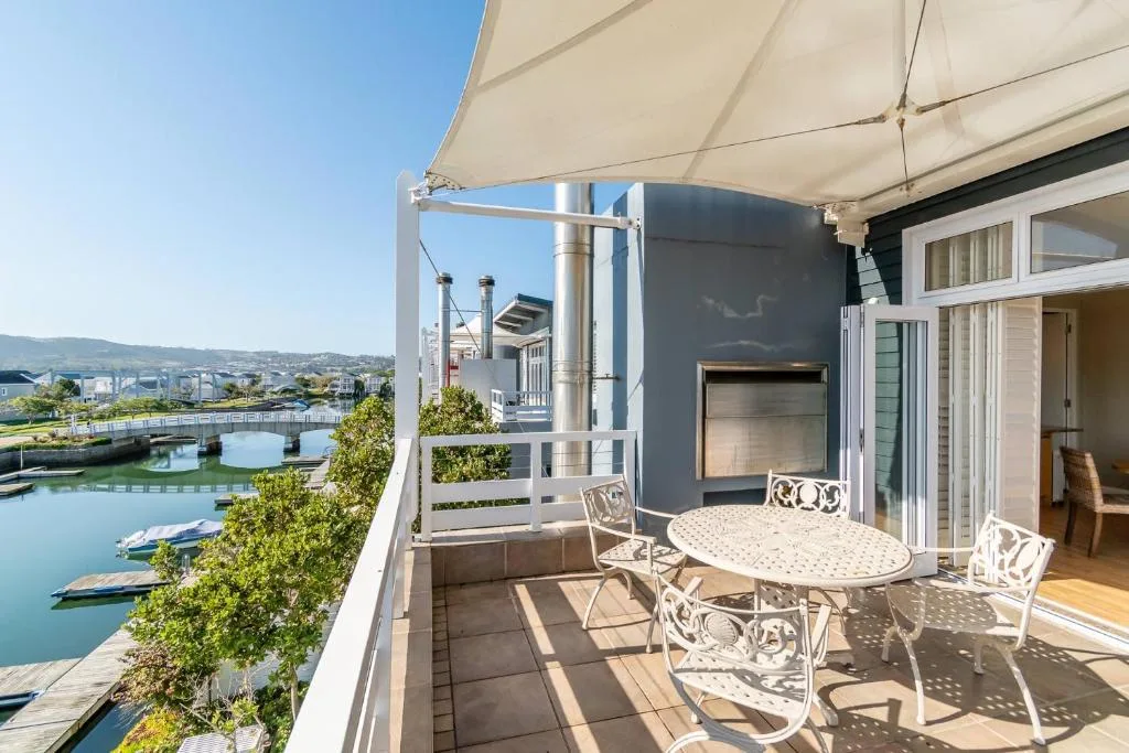 Spacious waterfront deck with dining table, umbrella, fireplace, and lagoon views