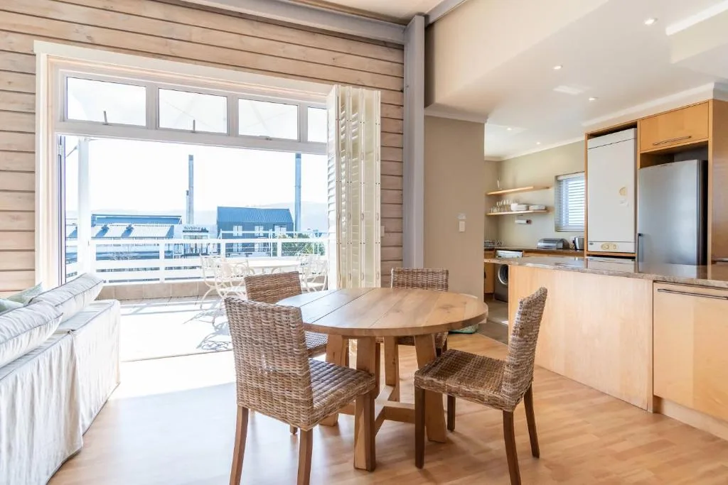 Open-plan dining area with round wooden table and wicker chairs, sea view beyond
