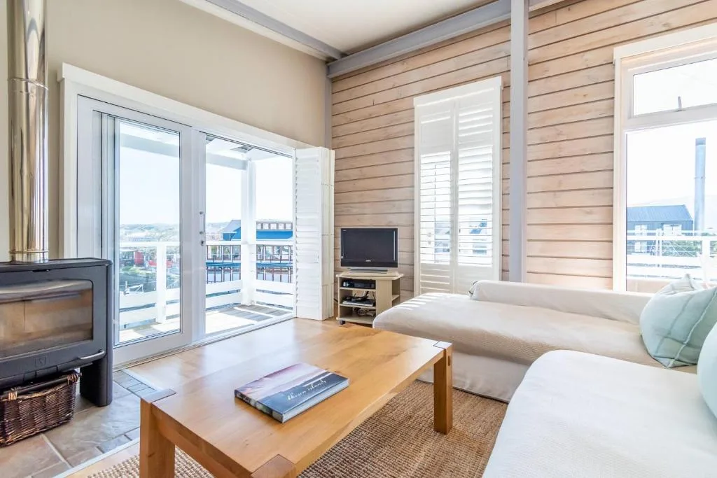 Spacious lounge with sofa, fireplace, TV, and scenic coastal views through glass doors