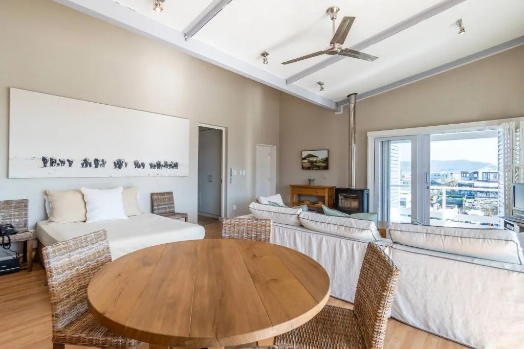 Modern open-plan lounge with round wooden table, cream sofas, and mountain views