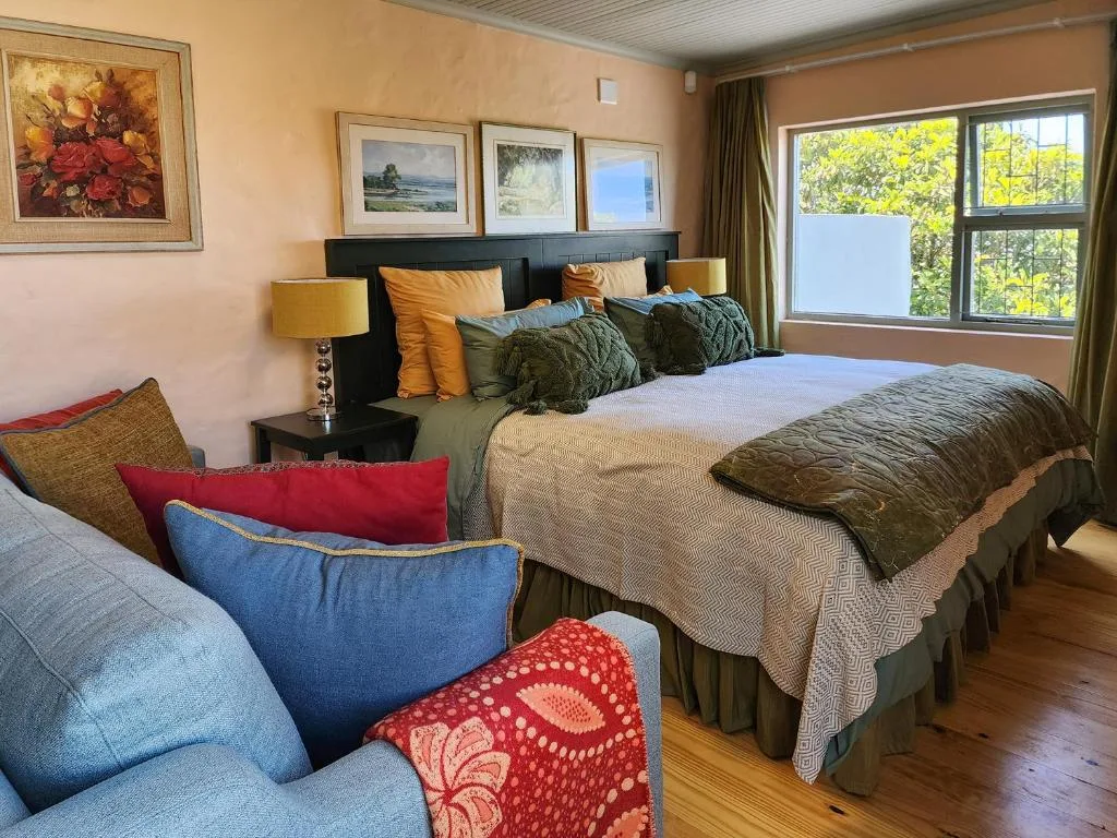 Spacious bedroom with queen bed, colorful pillows, and large windows overlooking greenery