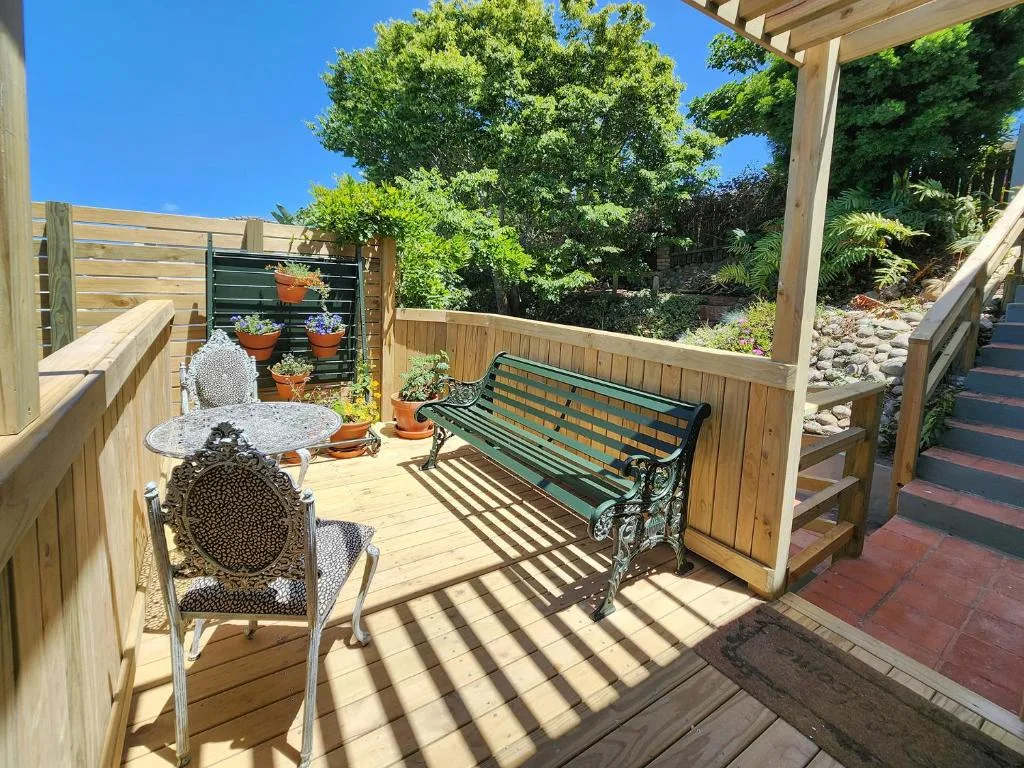 Wooden deck with green bench, chair, and potted plants under pergola