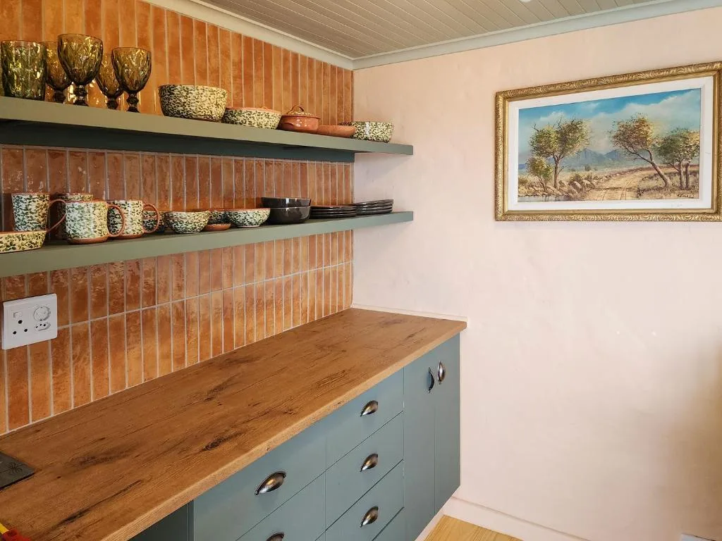 Modern kitchen with terracotta tile backsplash, wooden countertop, and decorative shelving