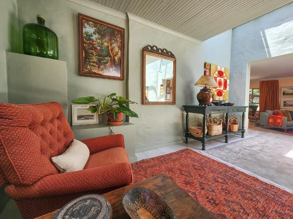 Spacious lounge with coral upholstered armchair, framed artwork, and decorative console table
