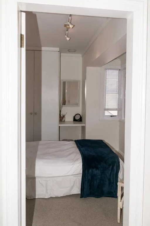 Compact bedroom with white bedding and dark throw blanket on single bed