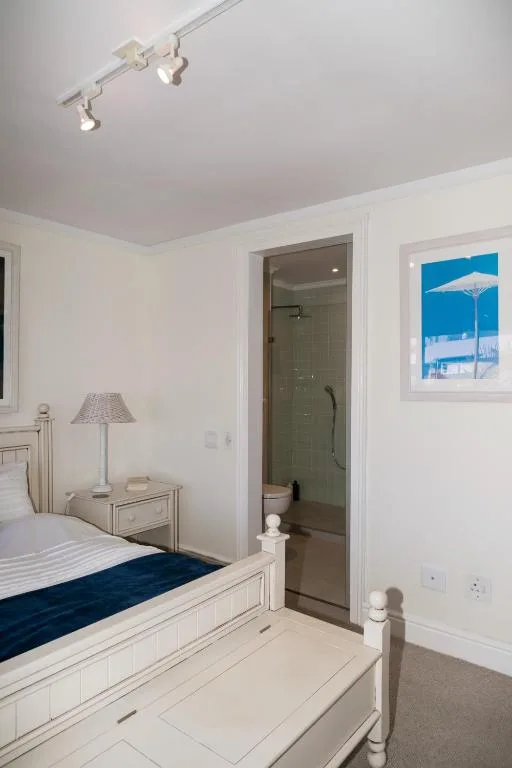 Bright bedroom with white furniture, bed with navy runner, ensuite bathroom visible