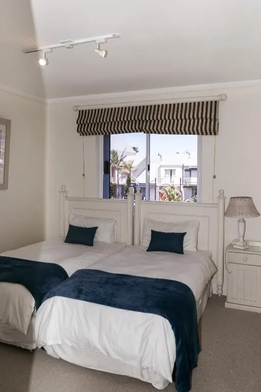 Bright bedroom with two beds, striped roman blind, and garden route views