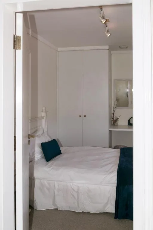 Compact bedroom with white bed, built-in wardrobe, and dark accent pillows