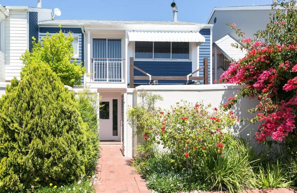 Modern waterfront house with blue deck, white walls, vibrant flowering plants