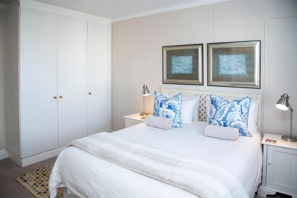 Bright bedroom with white bed, blue patterned pillows, framed artwork