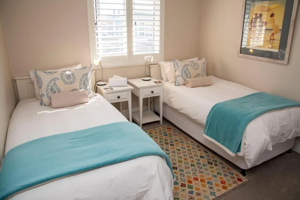 Twin bedroom with turquoise throws and patterned cushions, natural light from shuttered windows