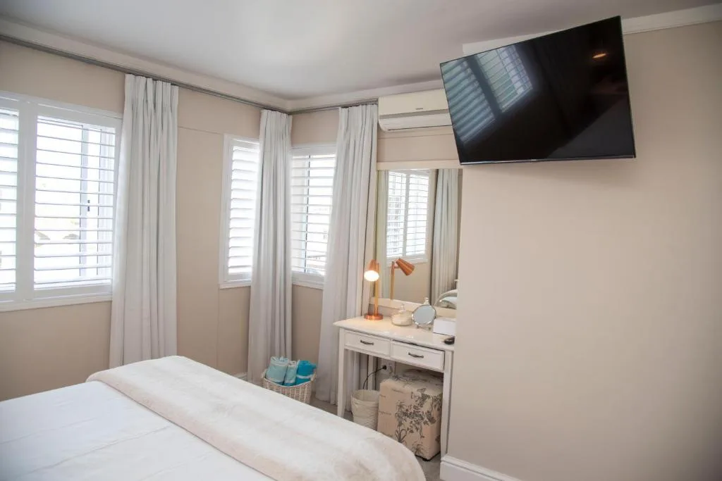 Bright bedroom with white shuttered windows, vanity desk, and wall-mounted television