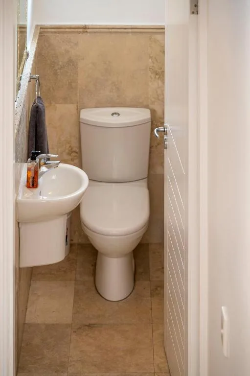 Compact bathroom with toilet, sink, and tiled walls in neutral tones
