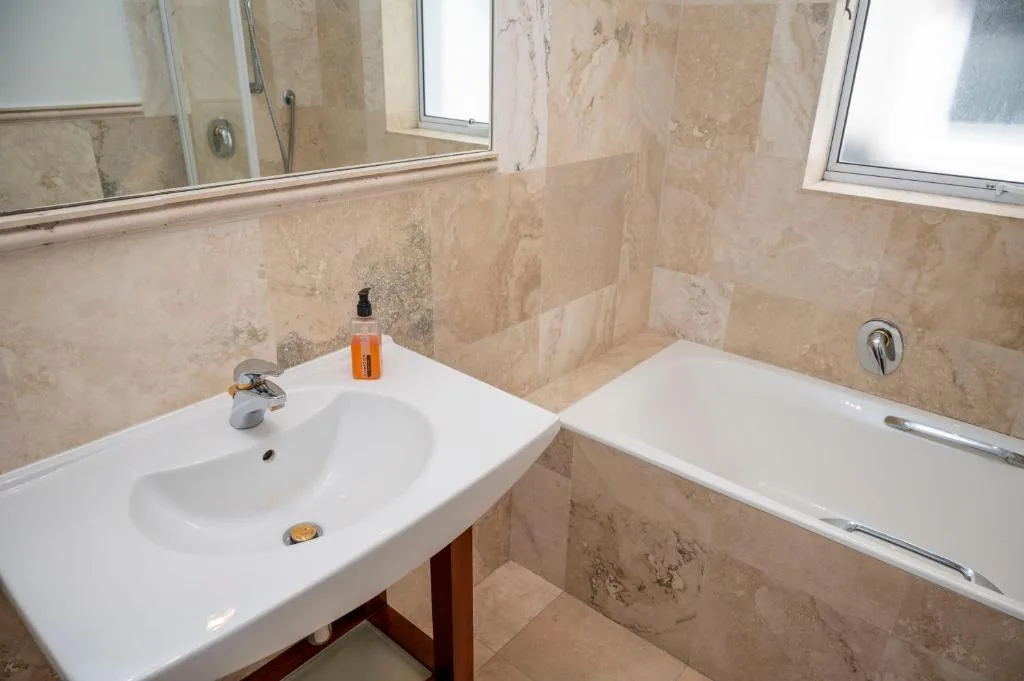 Modern bathroom with marble tiles, white sink and bathtub with fittings